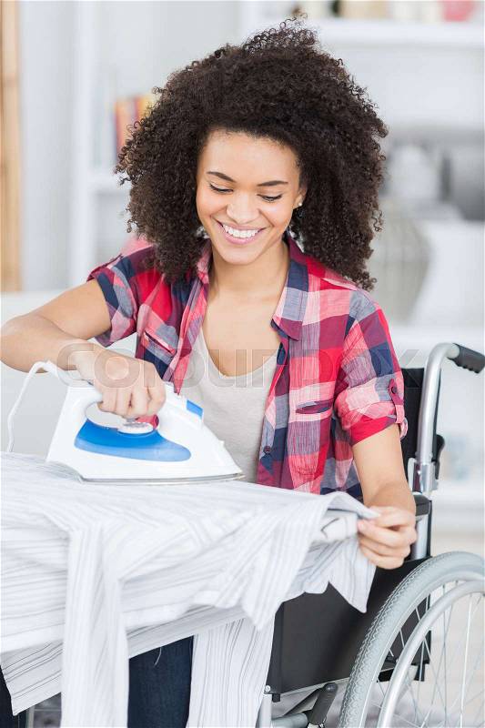 Happy woman on wheelchair during ironing at home, stock photo