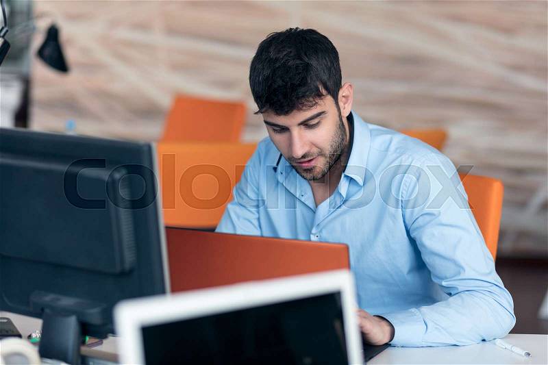 Happy young business man working on desktop computer at his desk in modern bright startup office interior, stock photo