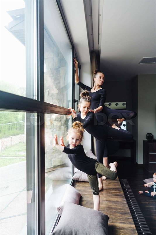 Mom and two daughters practice ballet at home by the window, stock photo