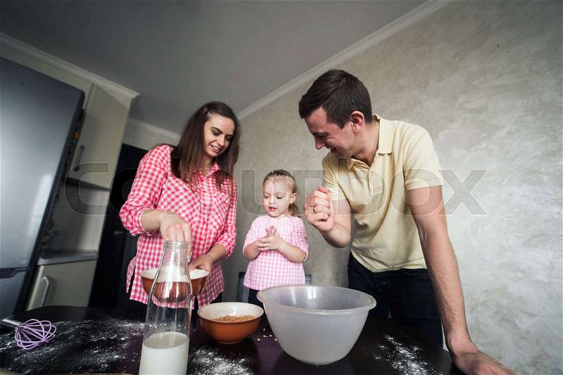 Mom, dad and little daughter in the kitchen play together with flour, stock photo