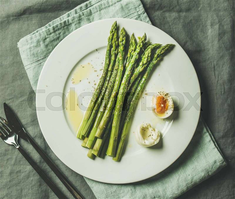 Cooked asparagus with soft-boiled egg and herbs on white round plate over grey textile background, top view. Clean eating food concept, stock photo