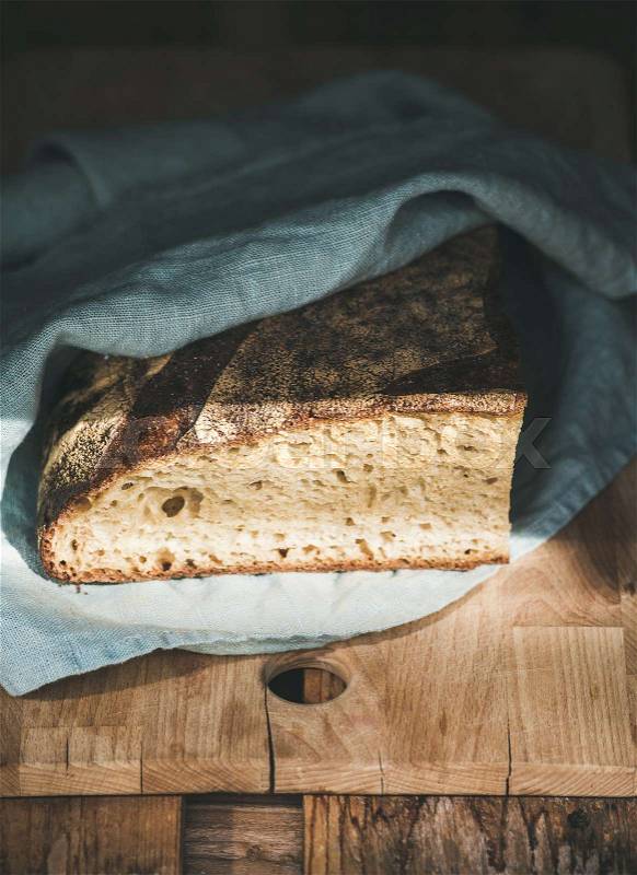 Rustic French rye bread loaf covered with kitchen towel over wooden board, selective focus. , stock photo
