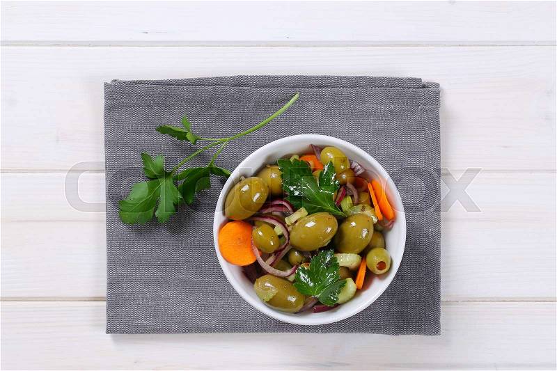 Bowl of vegetable salad with pickled green olives on grey place mat, stock photo