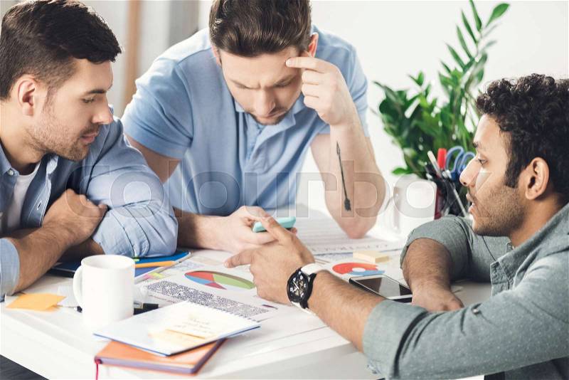 Three young businessmen sitting at table and working on new project together, business teamwork concept, stock photo