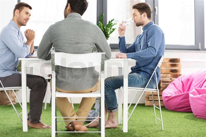 Three young businessmen sitting at table and working on new project together, business teamwork concept, stock photo