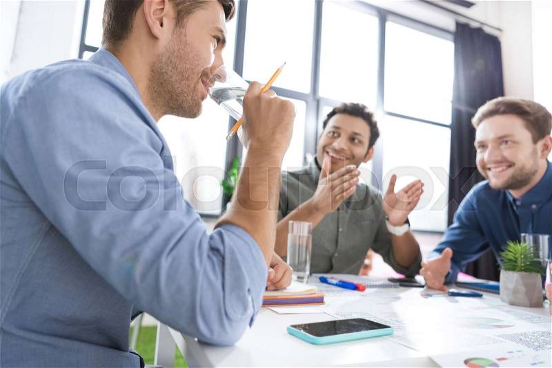 Smiling young businessmen drinking water and discussing new project, business teamwork concept, stock photo