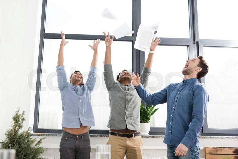 Cheerful young businessmen triumphing and throwing papers in office, business teamwork concept, stock photo