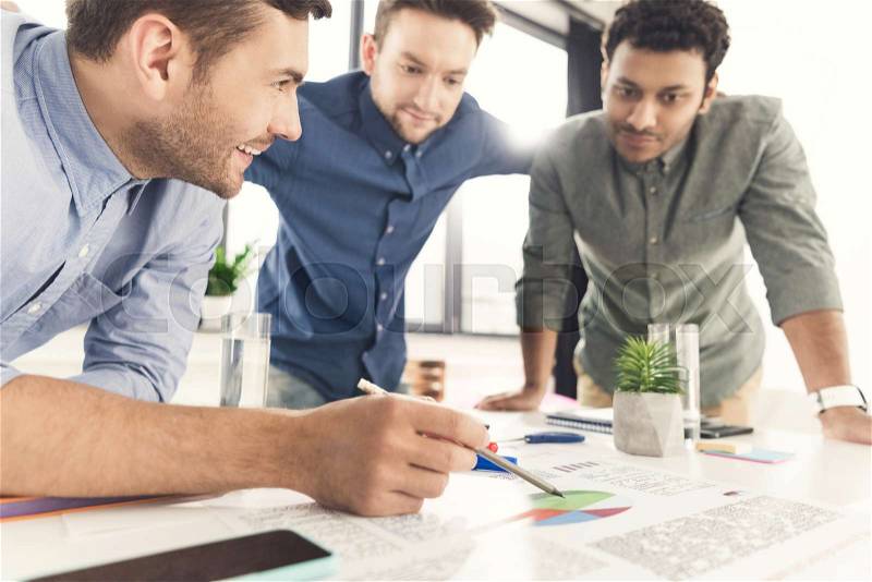 Three young businessmen leaning at table and working at project together, business teamwork concept, stock photo