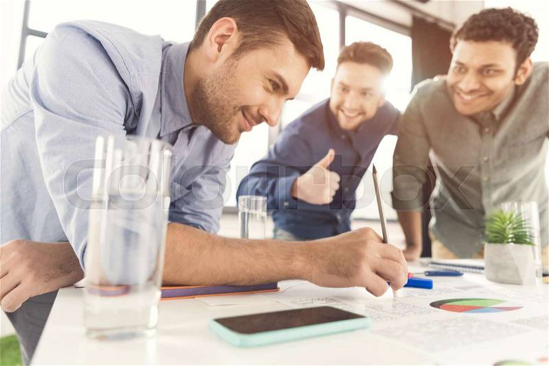 Three young businessmen leaning at table and working at project together, business teamwork concept, stock photo