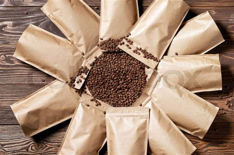 Many mock-up craft paper pouch bags top view over wooden background with coffee beans in the center, stock photo