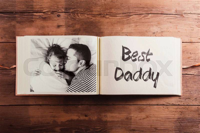 Fathers day concept. Photo album, black-and-white picture of daughter lying in bed, her father kissing her on cheek. Studio shot on wooden background, stock photo