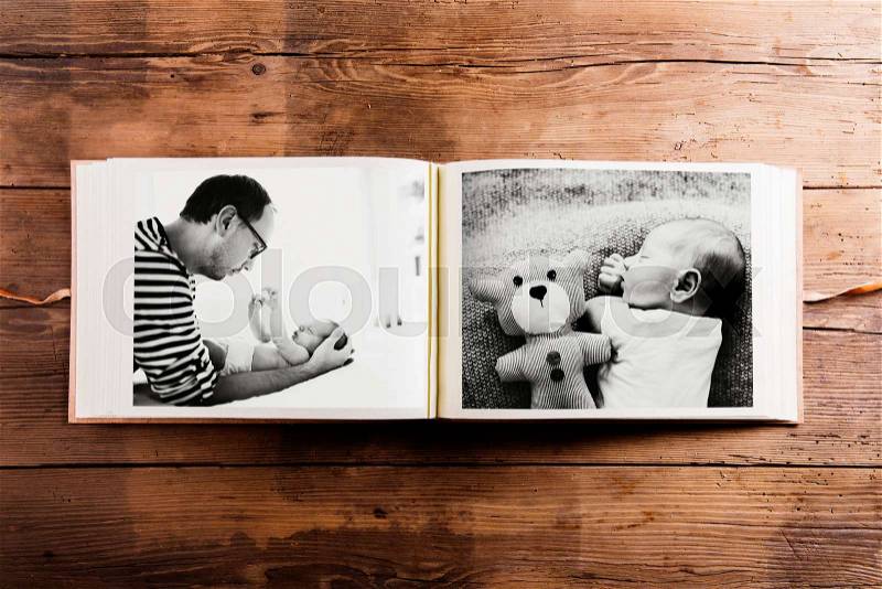 Photo album with pictures of young father and his cute newborn baby son. Fathers day concept. Studio shot on woden background, stock photo