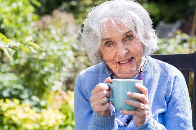 Portrait Of Senior Woman Relaxing In Garden With Hot Drink, stock photo