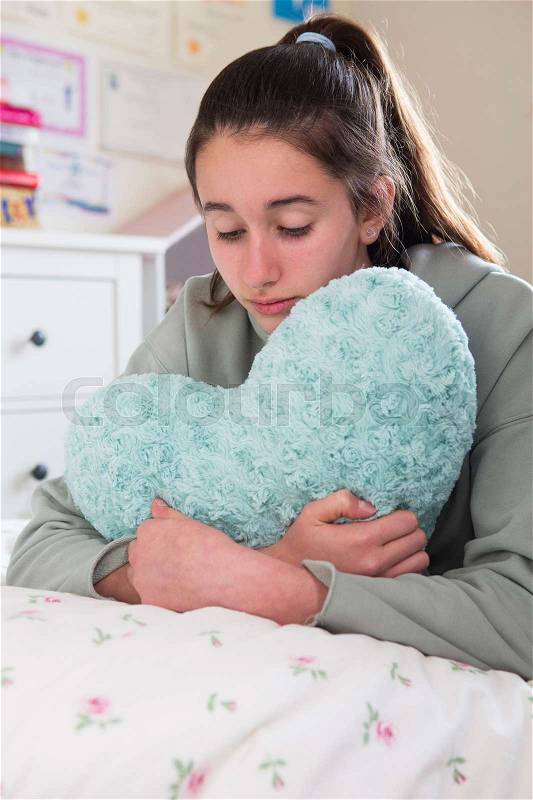 Young Girl Lying On Bed Hugging Heart Shaped Cushion, stock photo
