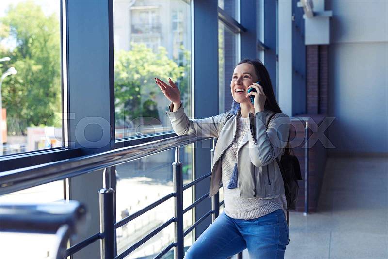 Wide shot of female exited with conversation on phone while leaning on handrail, stock photo
