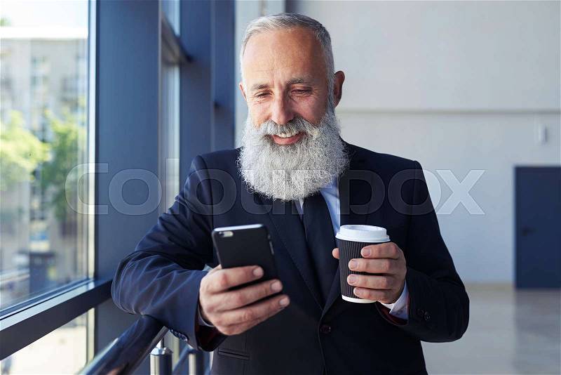 Mid shot of solid man holding cup of coffee and surfing in phone with copy space, stock photo