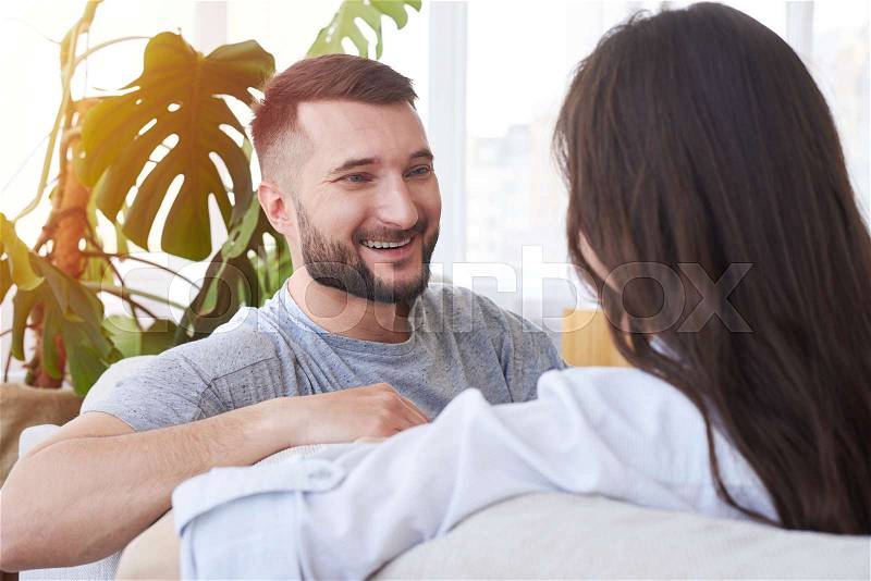Over-the-Shoulder Shot of brunette and bearded man chatting while having rest on sofa, stock photo