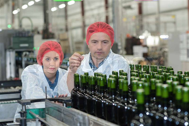 Workers examining wine bottles at bottling plant, stock photo