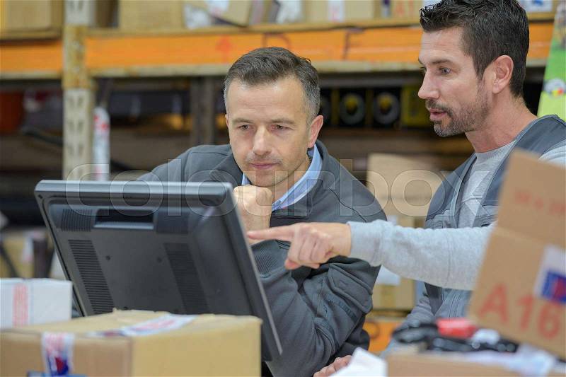 Warehouse worker and manager using computer in a warehouse, stock photo