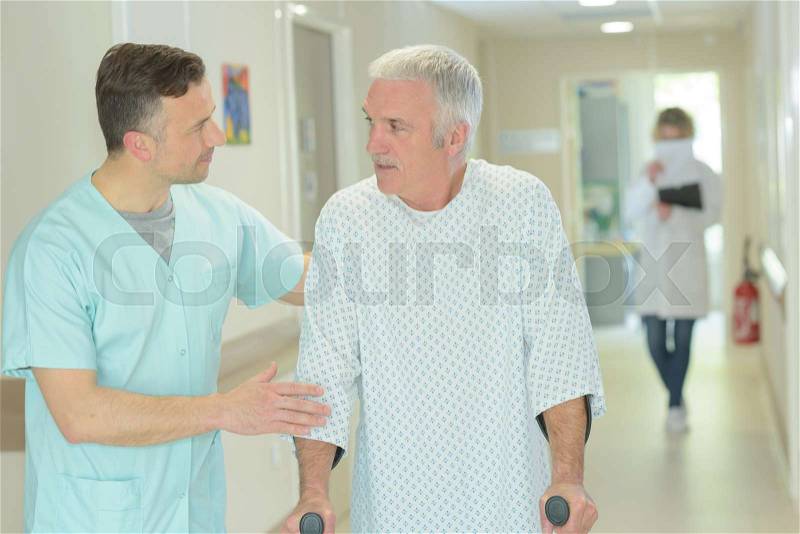 Male doctor is helping older patient with crutches, stock photo