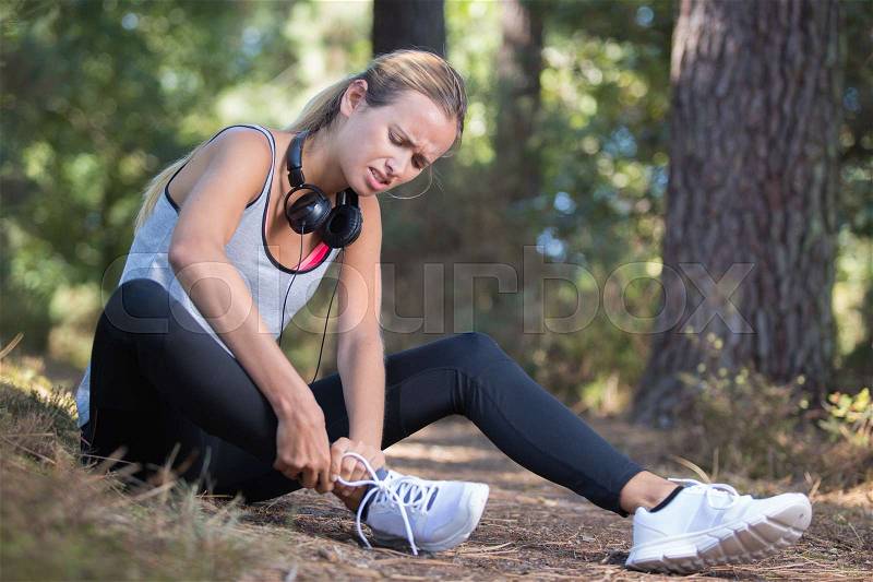Female runner touching foot in pain due to sprained ankle, stock photo