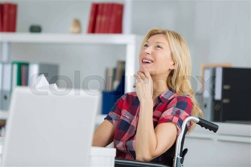 Happy woman on wheelchair using digital tablet at home, stock photo