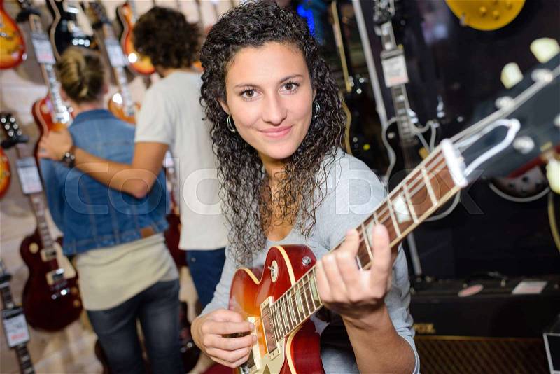 Smiling female customer trying to play guitar in store, stock photo
