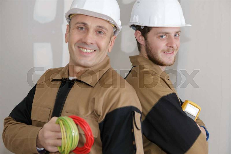 Smiling handyman with rolled wire and apprentice, stock photo