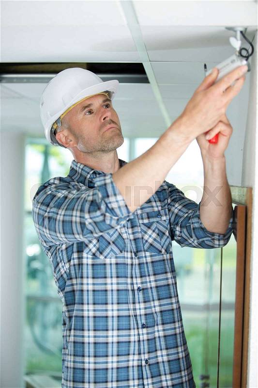 Male technician installing camera on wall using electric cordless drill, stock photo