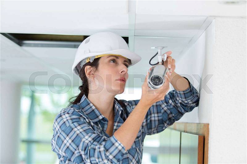 Female technician installing camera on wall with screwdriver, stock photo