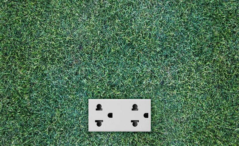 Double plug socket on the wall on green grass background, stock photo