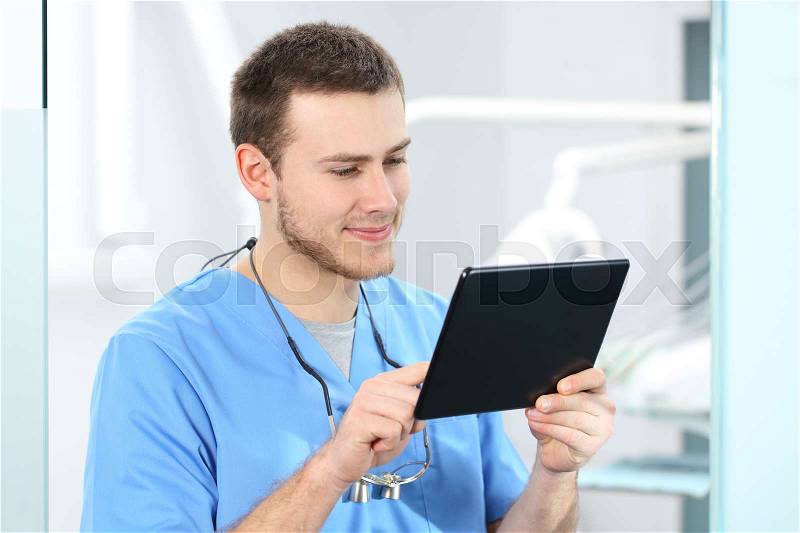 Doctor wearing blue coat working on line with a tablet in a dentist office, stock photo