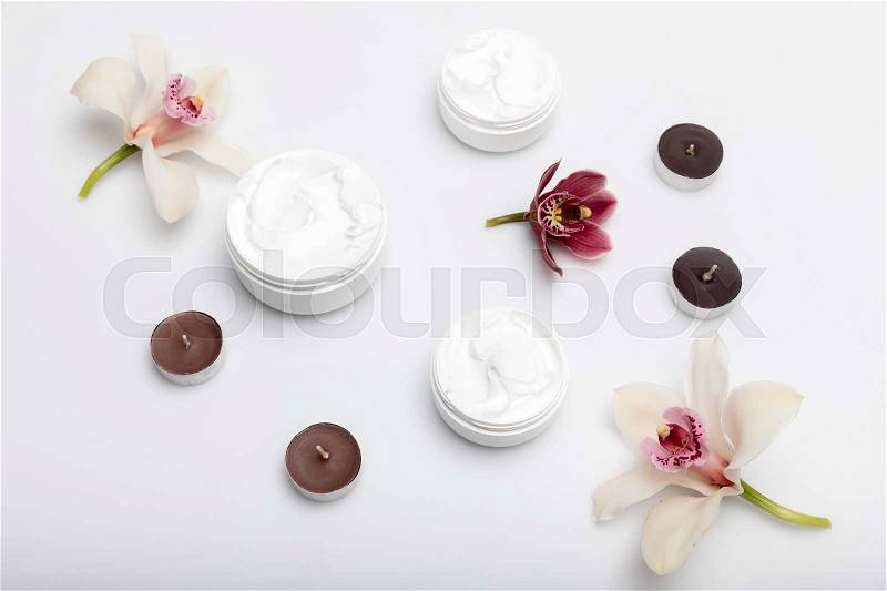 Close-up view of organic cream in containers with orchids and candles isolated on white , stock photo