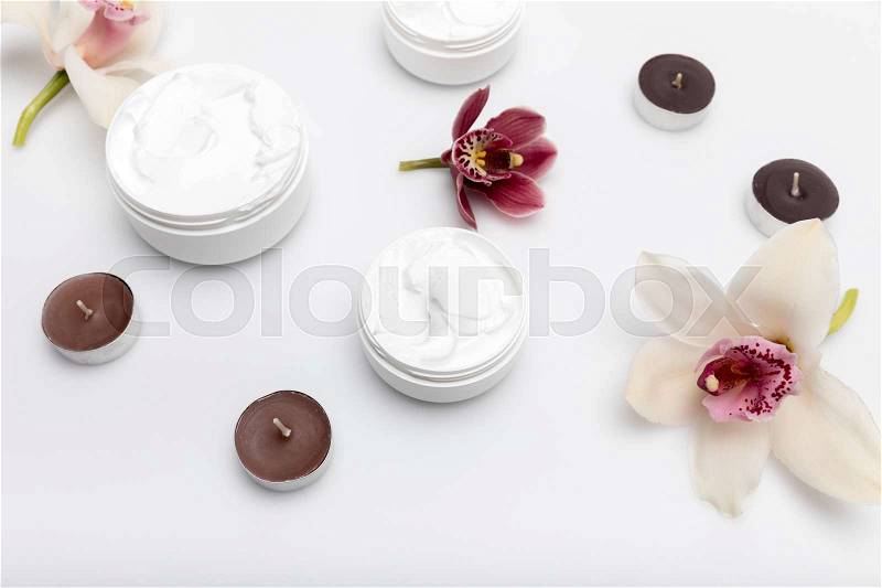 Close-up view of organic cream in containers with orchids and candles isolated on white, stock photo