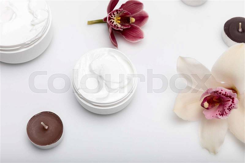 Close-up view of organic cream in containers with orchids and candles isolated on white , stock photo