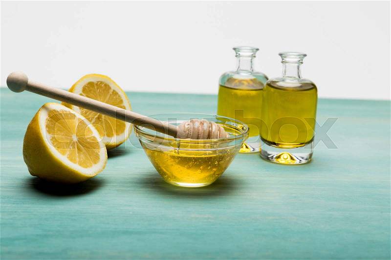 Close-up view of essential oil in small bottles, honey in bowl and sliced lemon on wooden table, stock photo