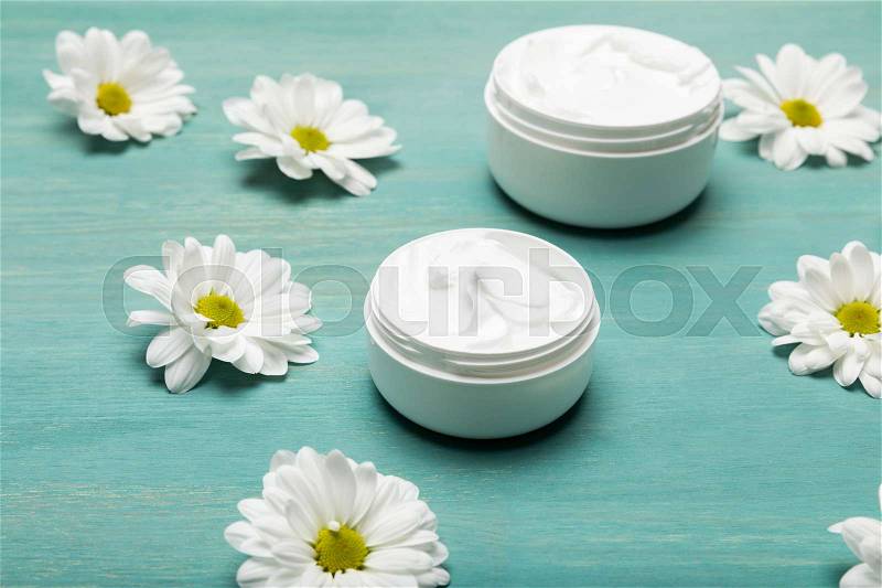 Close-up view of organic cream in containers and chamomiles on blue wooden table , stock photo