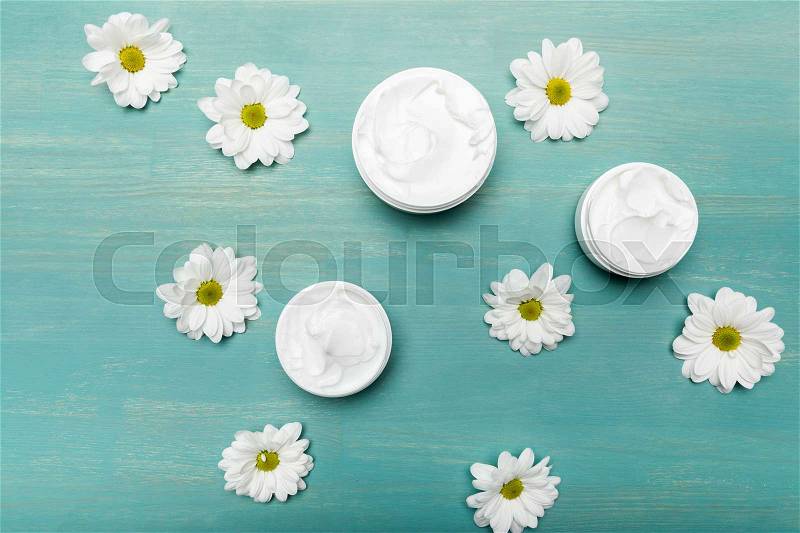 Top view of organic cream in containers and chamomiles on blue wooden table , stock photo