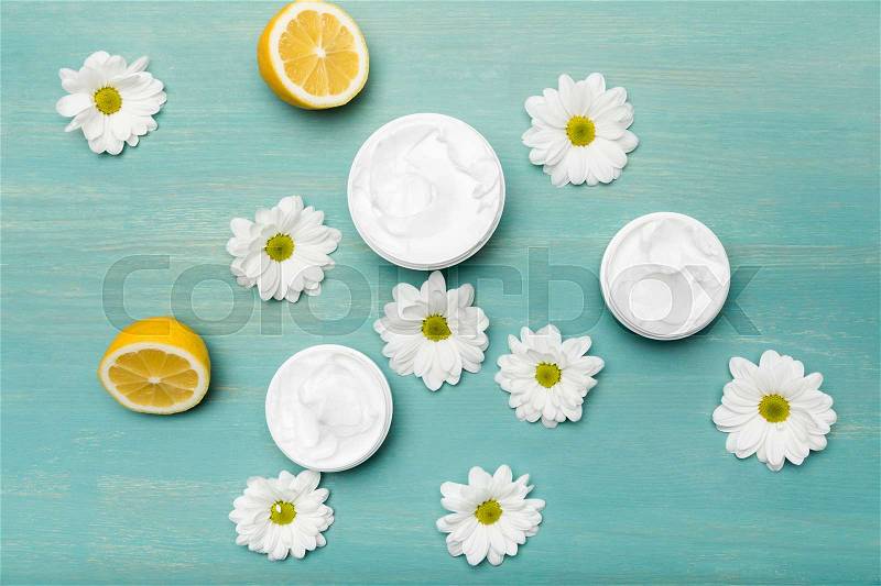 Top view of natural cream in containers, chamomiles and sliced lemon on blue wooden table, stock photo