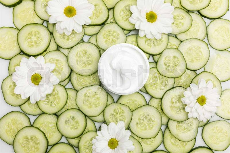 Top view of facial cream in container and cucumber slices with chamomiles , stock photo