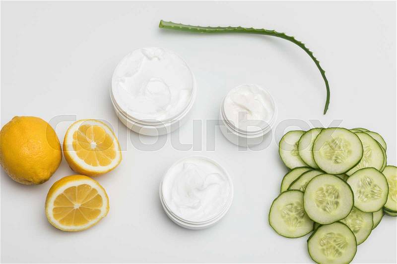 Top view of facial cream in containers, cucumber and lemon slices and aloe vera plant isolated on white, stock photo