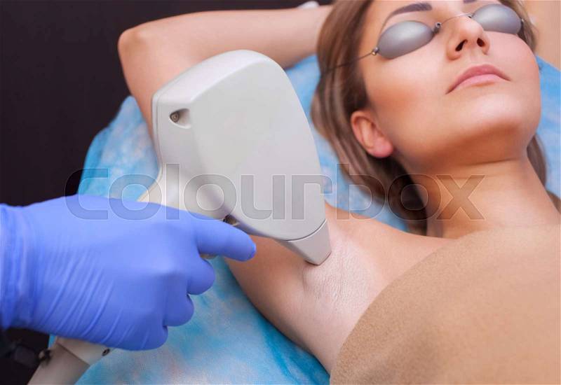 The cosmetologist does the laser hair removal procedure in the armpit zone, to a young woman in a beauty salon, stock photo