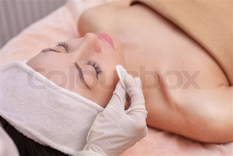 The doctor cosmetologist cleanses with a tonic the face skin of a beautiful, young woman in a beauty salon.Cosmetology skin care, stock photo