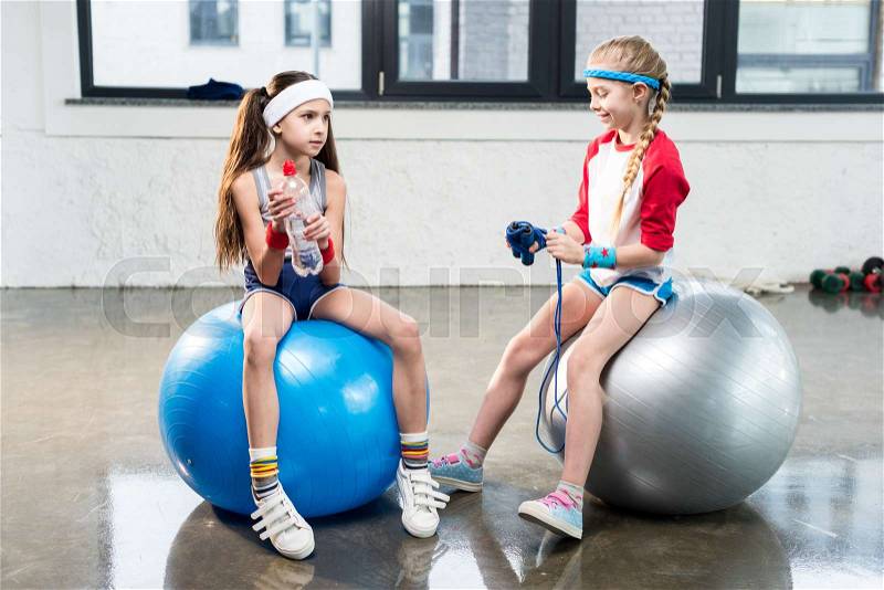 Two little girls in sportswear sitting at fitness studio, children sport concept, stock photo