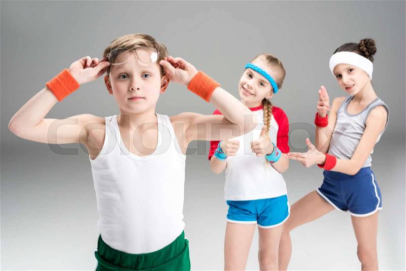Little boy in sportswear adjusting eyeglasses and sporty girls standing behind, children sport concept, stock photo