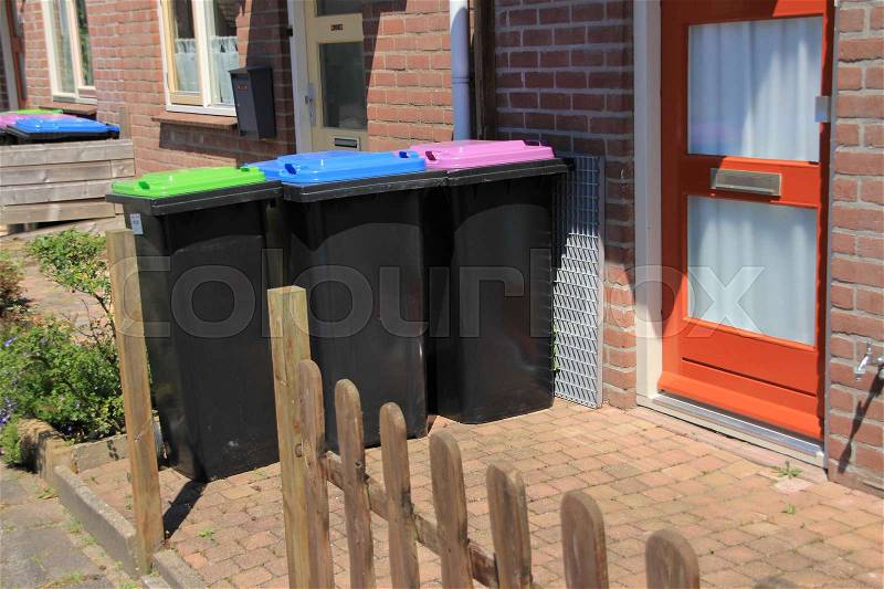 Three waste containers with different colours of the covers for recycling in the front garden in the residential area in the village on a sunny day, stock photo