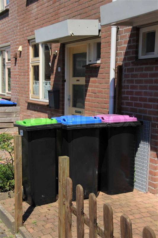 Three waste containers with different colours of the covers for recycling in the front garden in the residential area in the village on a sunny day, stock photo