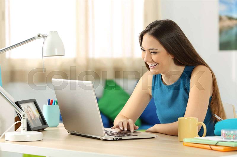 Single student searching content in a laptop sitting on a desk in her room, stock photo