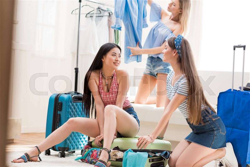 Young women packing suitcases for vacation together at home, packing luggage concept, stock photo