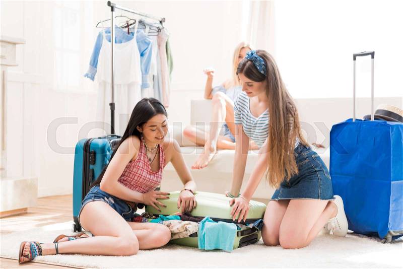 Young women packing suitcases for vacation together at home, packing luggage concept, stock photo